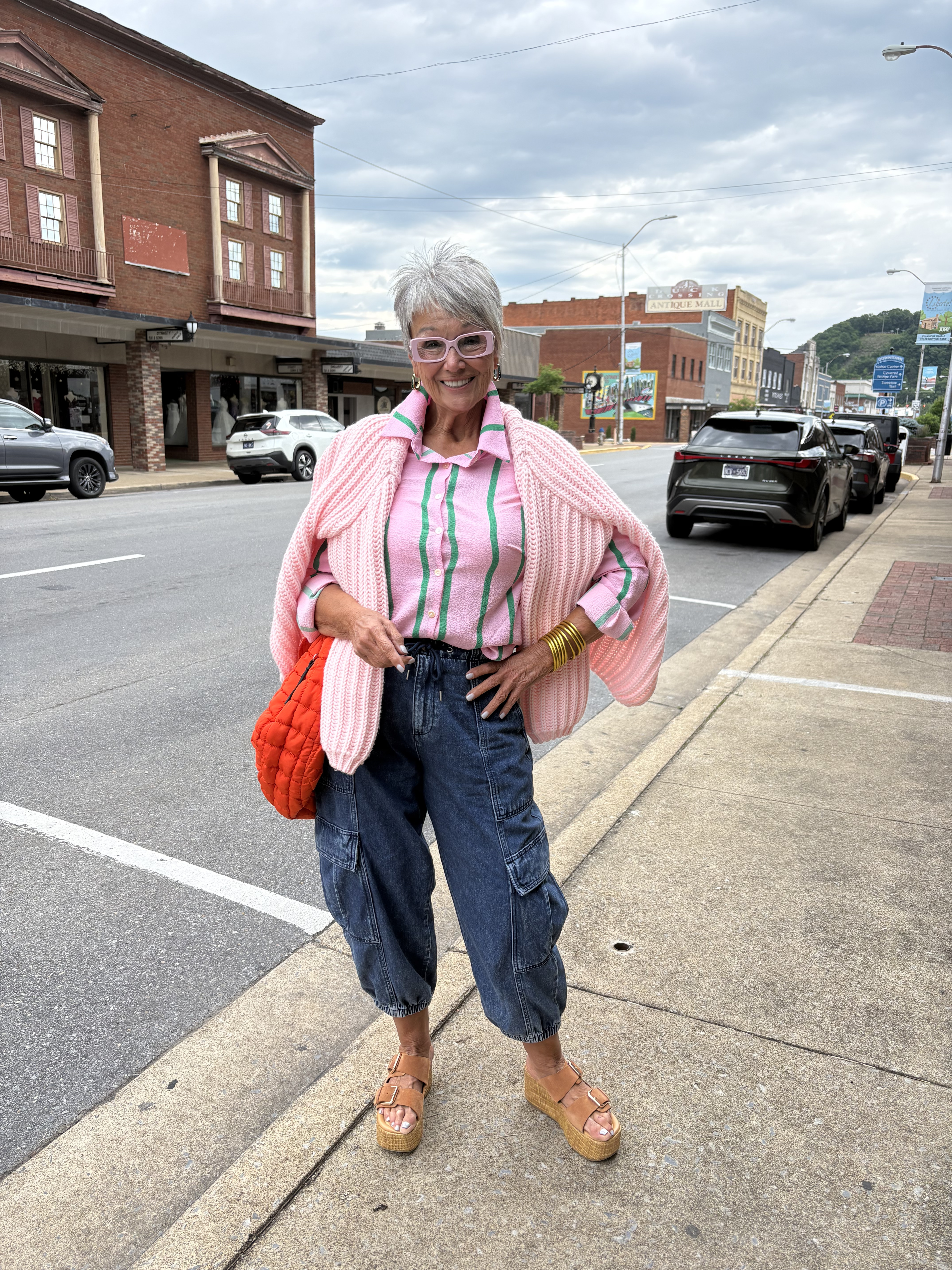 Mindy in a pink cardigan and cargo jeans on a downtown street, holding an orange bag